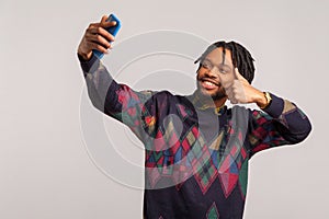 Satisfied smiling african man with dreadlocks and beard showing thumbs up looking at camera of mobile phone, video call,