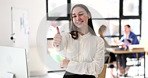 Satisfied smiling business woman or female student showing thumbs up in office