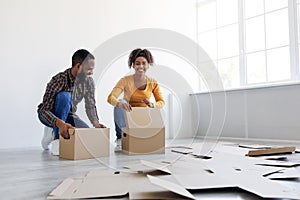 Satisfied smiling millennial african american husband and wife stack cardboard boxes, packing stuff and prepare to move