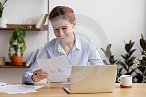Satisfied smiling woman sitting at desk working with business papers