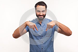 Satisfied successful man with beard pointing fingers down paying attention at advertising area, showing freespace, looking at