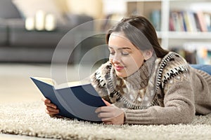 Satisfied teen in winter reading paper book at home