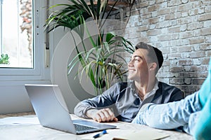 Satisfied teenager happy to finish work with laptop at home, raises hands and puts feet up on table, relaxing after hard working