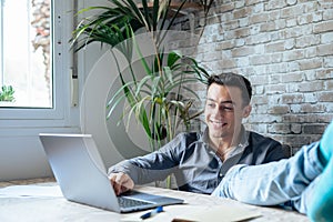 Satisfied teenager happy to finish work with laptop at home, raises hands and puts feet up on table, relaxing after hard working