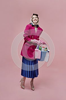 A satisfied woman holds a bucket of cleaning tools in her hands, full-length.