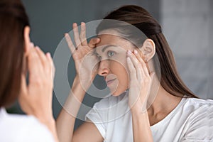 Satisfied woman looking in mirror check face after beauty treatment