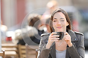 Satisfied woman smelling a cup of coffee on a terrace