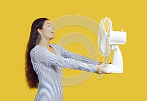 Satisfied woman suffering from heat enjoys cold air from electric fan on yellow background.