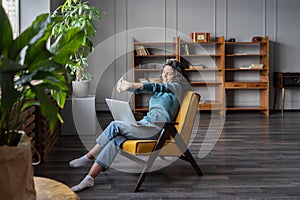 Satisfied with work done woman stretch hands relax sit in cozy armchair with laptop in home office