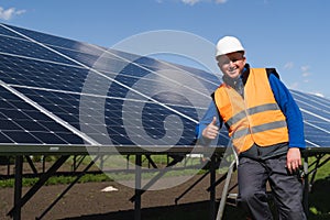 Satisfied worker showing thumb up gesture while standing near solar panels at power plant.