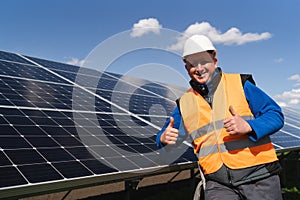 Satisfied worker showing thumbs up gesture while standing near solar panels at power plant.