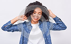 Satisfied young African American woman dressed in blue denim shirt, holding hands on head, feels happy. Positive African American