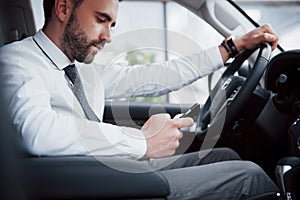 Satisfied young business man looking at mobile phone while driving a car