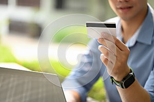 Satisfied young man holding credit card making purchase or payments on laptop computer