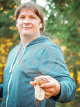 Satisfied young man holding a found porcini mushroom in his hands. The mushroom picker holds a cep mushroom. Man collect