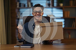 Satisfied young man sitting at workdesk, holding delivery box, gesturing