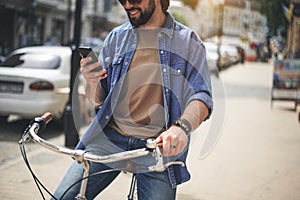 Satisfied young man taking seat on bicycle with phone