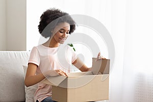 Satisfied young woman customer sit on sofa, unpack package parcel