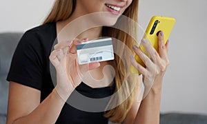 Satisfied young woman doing online transaction with her smartphone and credit card comfortably from home. Online shopping and