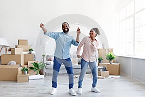 Satisfies excited young african american lady and guy dancing in living room with cardboard boxes with things