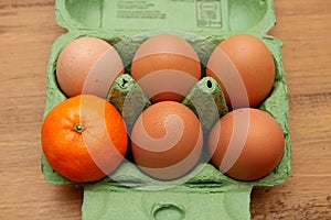 Satsuma, or small orange, in an egg carton, alone with five eggs