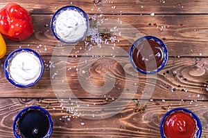 Sauce in the assortment on a brown wooden background, decorated with pepper, cherry tomatoes, spices, coarse salt