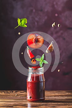 Sauce components frozen in the air. Homemade plum sauce chutney with chilli or tkemali in glass jar standing on wooden table with