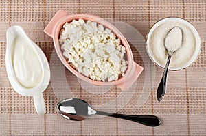 Sauceboat with sour cream, pink bowl with cottage cheese, teaspoon in bowl with sugar, spoon on napkin. Top view
