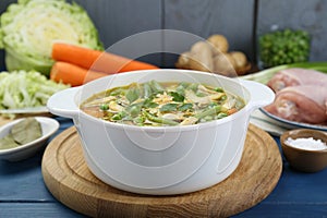 Saucepan of delicious vegetable soup with chicken and different ingredients on blue wooden table