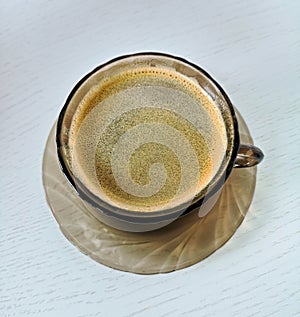 Saucer and cup of tempered brown glass with black coffee stand on a white wooden table