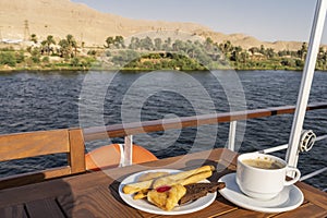 A saucer with cupcakes, pastries and a cup of coffee stands on a wooden table on the deck of a cruise liner.