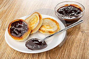 Saucer with small pancakes with chocolate sauce, teaspoon, bowl with chocolate sauce on table