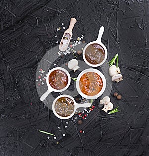 sauces in cups on a black background. different sauces of red and orange color on a black stone board with spices