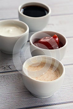 Sauces ketchup, mustard, mayonnaise, sour cream, soy sauce in clay bowls on wooden white background