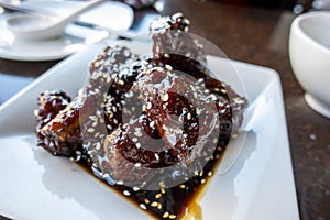 Saucy baby back pork ribs on a white square plate inside an Asian restaurant