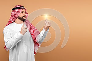 A Saudi Arab man holds a light bulb in his hand as a symbol of the idea in national dress. Dishdasha, kandora, thobe, islam. Copy