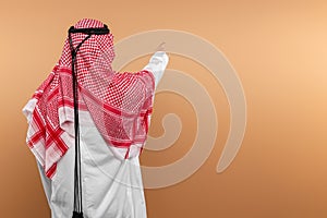 A Saudi Arab man in national dress points his finger at free space. Dishdasha, kandora, thobe, islam. Copy space