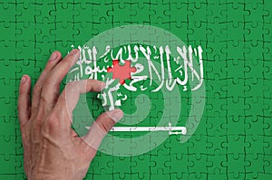 Saudi Arabia flag is depicted on a puzzle, which the man`s hand completes to fold