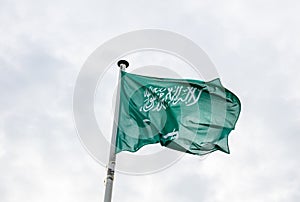 Saudi Arabia flag on a pole waving, cloudy sky background