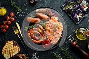 Sauerkraut and grilled sausages with rosemary and cranberries on a black plate. Traditional German dish.