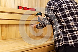 Sauna construction - man screwing wooden bench backrest photo
