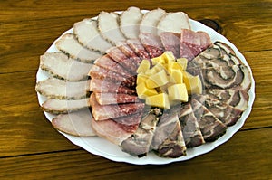 Sausage, baked meat, roll and cheese in a white plate on a wooden background