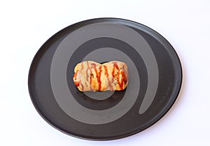 Sausage bread roll and mayonnaise with ketchup and dried oregano topping in the black round plate