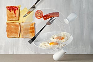 Sausage with a circle of tomato are balancing on a fork with a plate of fried eggs on a hodgepodge against a background of bread photo