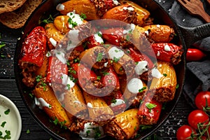 Sausage meat, mince and rice Stuffed sweet mini bell peppers baked in cast iron skillet, pan topped with yogurt and fresh parsley