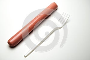 Sausage next to a fork on a white background. Copy space. The concept of fast food, GMOs, hunger or lack of food. Environmental