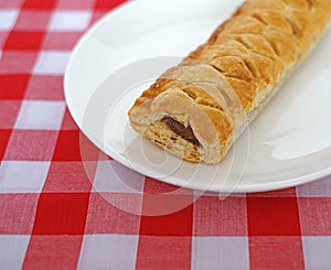 Sausage roll on a white plate on red and white checked table cloth