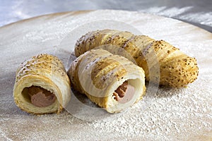 Sausage Rolls With Sesame Cut in Half on Floury Wooden Table