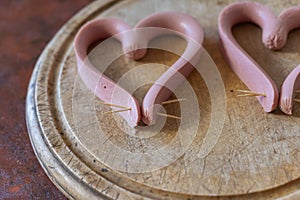 Sausages cut lengthwise are laid out on a cutting board. The sausages are laid out in the shape of a heart. Cooking the meal. Love