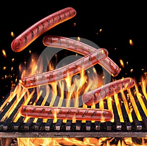 Sausages falling on the burning grill grate and tongues of fire flame